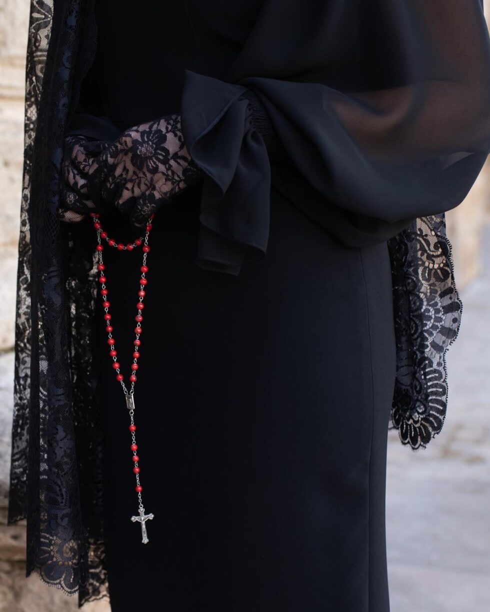 Vestido Noelia de Lyubasha Kyleshko en crepé elástico negro con mangas de gasa y puños fruncidos, detalle de guantes de encaje y rosario rojo para Semana Santa