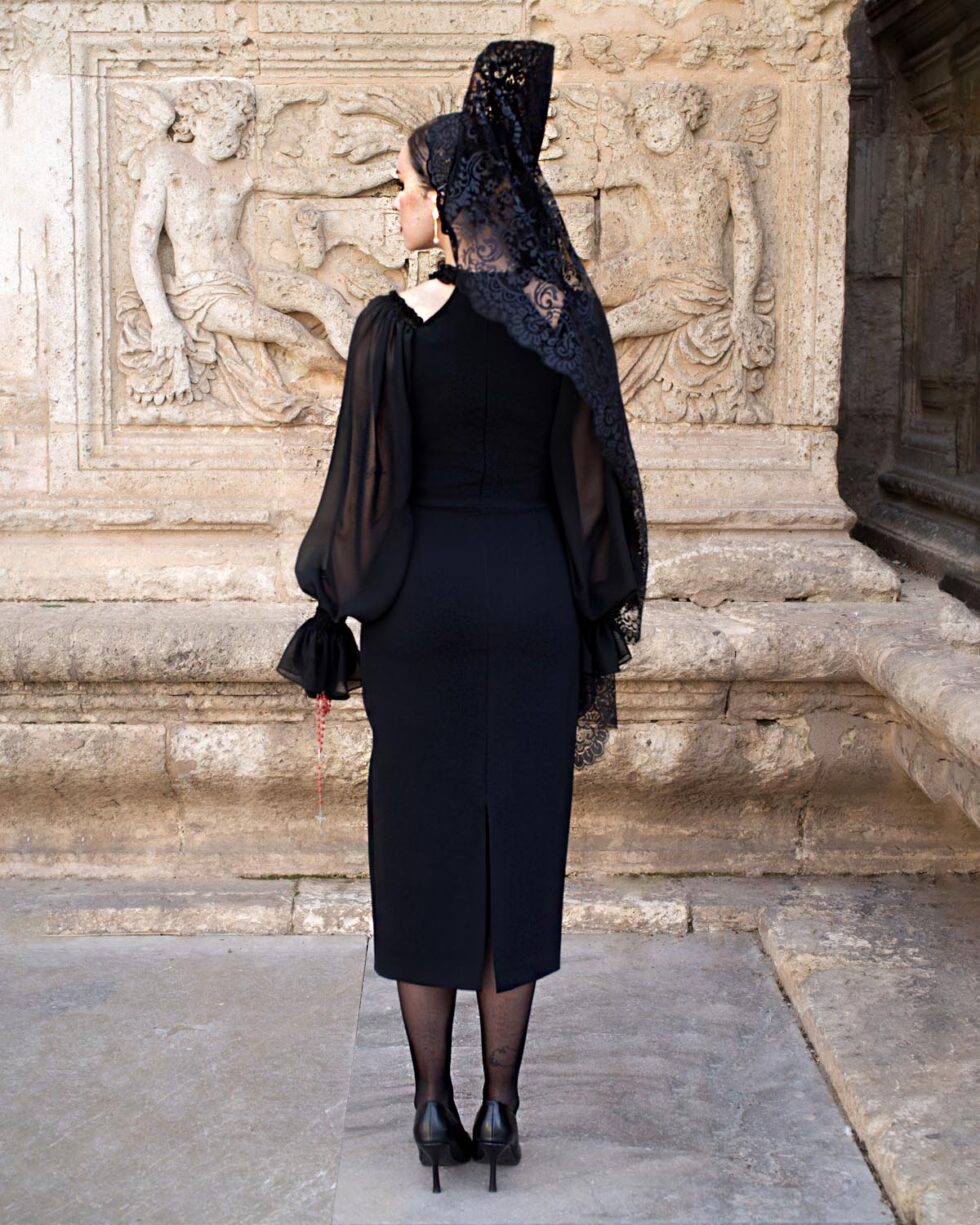 Vista trasera del vestido Noelia en crepé elástico negro con mangas de gasa y abertura central trasera, diseño entallado midi para actos solemnes